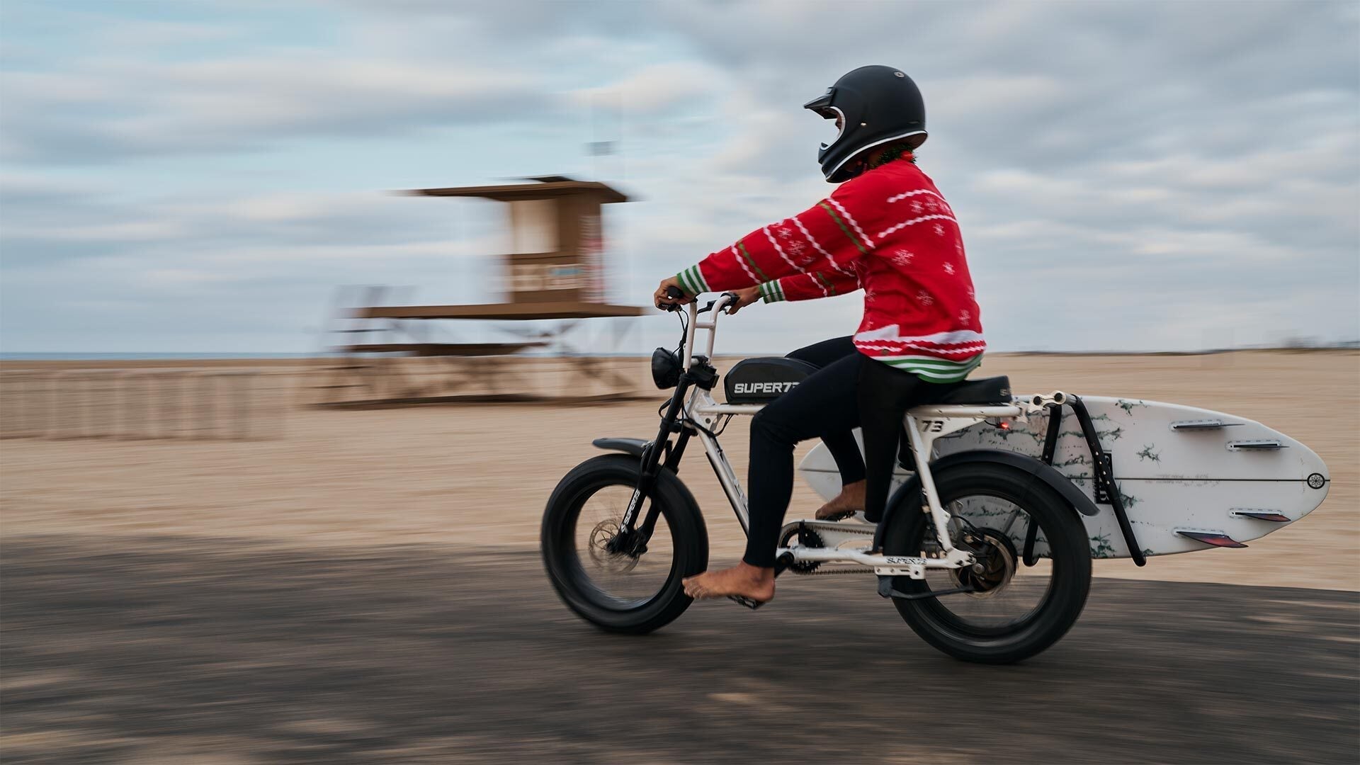 Rider in a holiday sweater at the beach riding a SUPER73 ebike