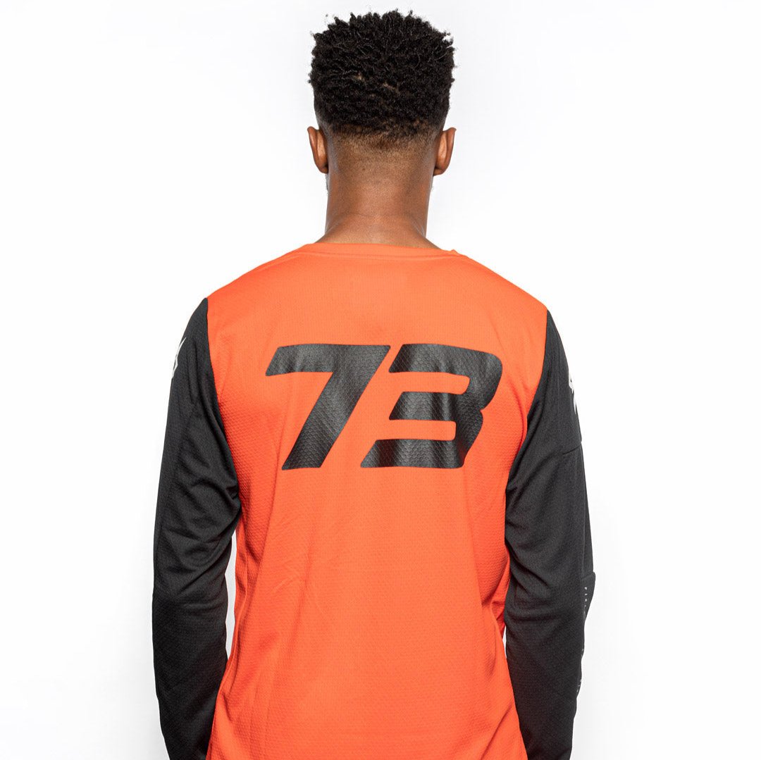 Male model back view of orange Premium long sleeve athletic moto hoon jersey. @color_blood orange