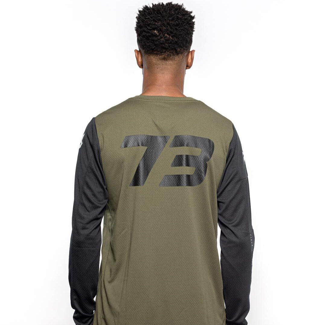 Male model back view of black and olive Premium long sleeve athletic moto hoon jersey. @color_dark fatigue