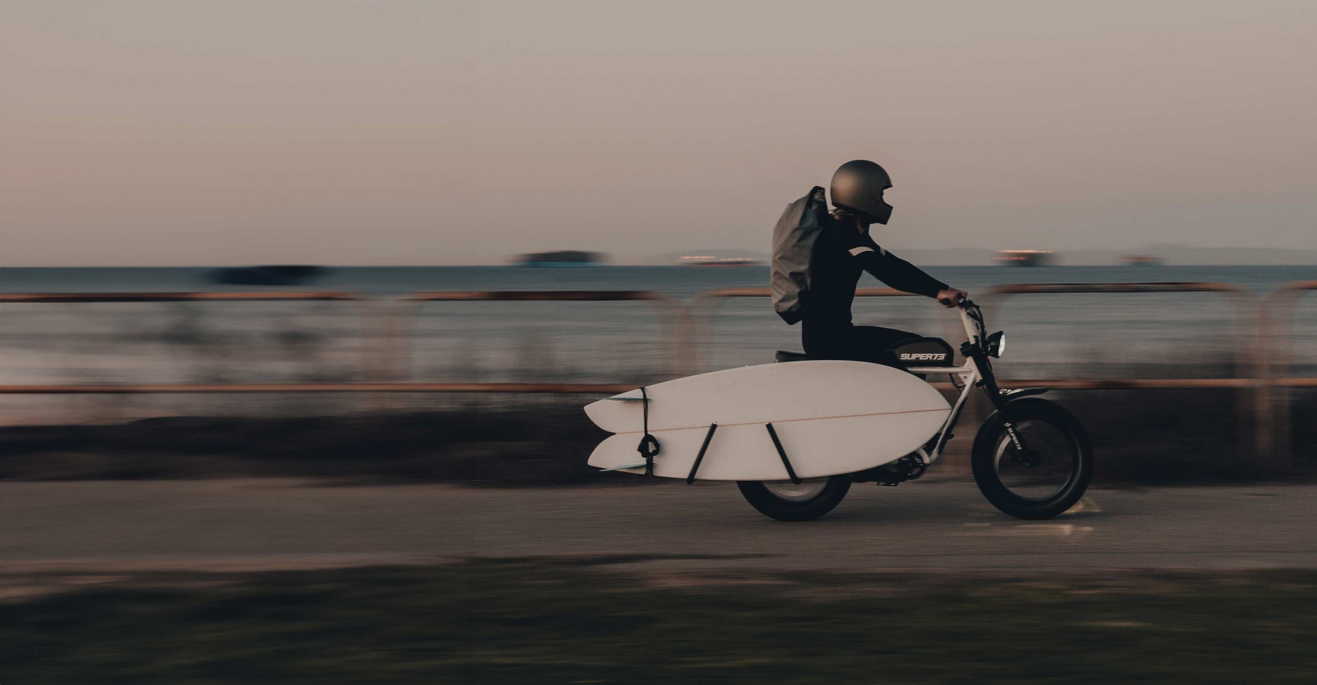 a surfer on his SUPER73 riding to the beach with his surf rack and surfboard.