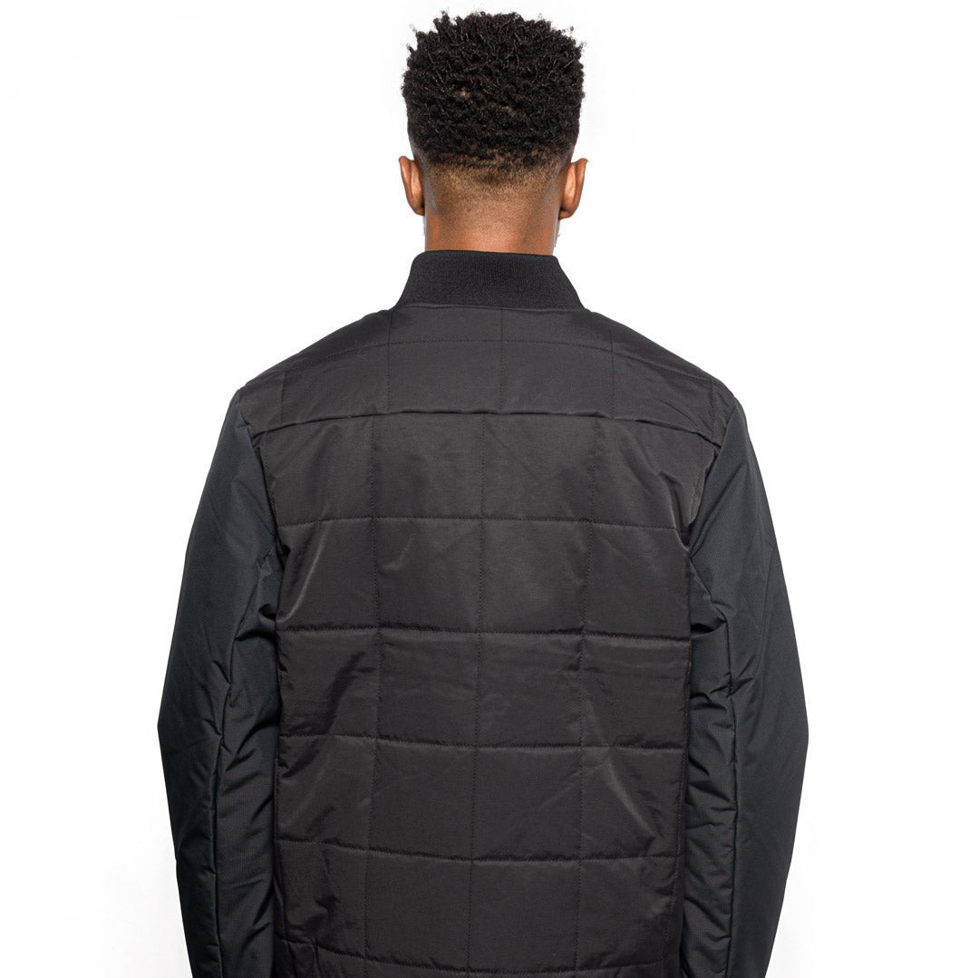 Back view of Male model wearing Sipes Varsity Jacket in black colorway. @color_black